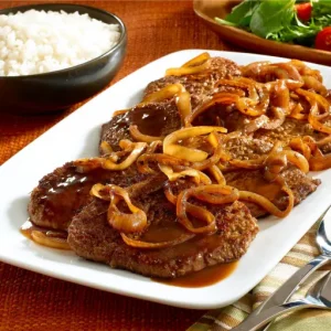 Tender breaded steak, cooked to golden perfection, is served alongside a fresh salad, fluffy rice, and crispy French fries.